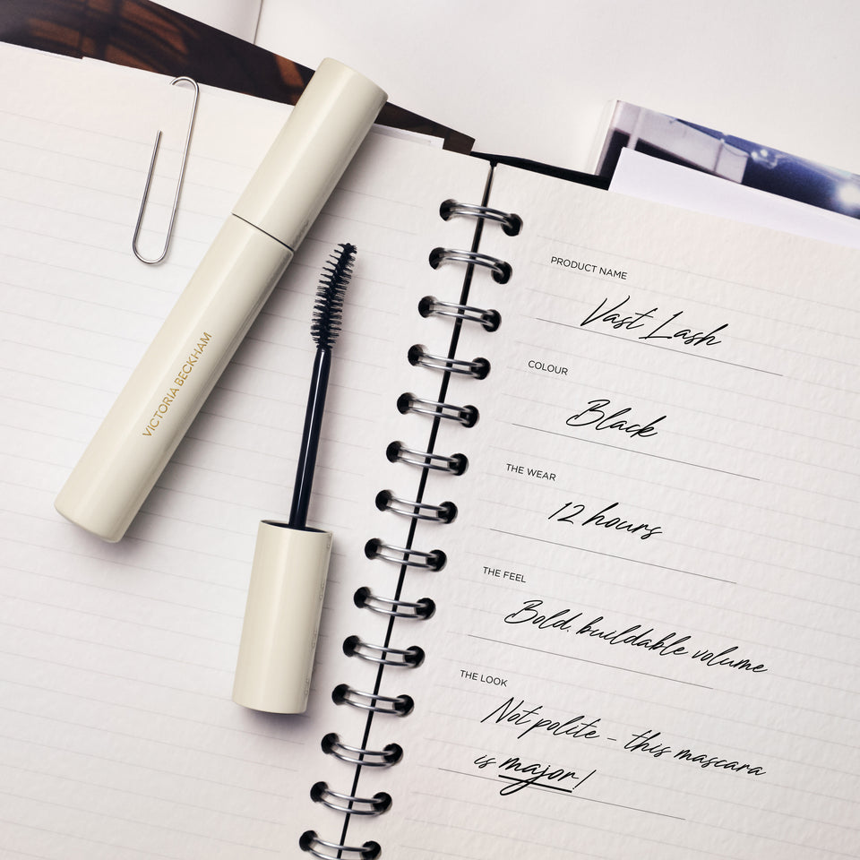 Vast Lash mascara in Black with wand pulled out, lying on a spiral notebook — Victoria Beckham Beauty's buildable volume mascara.