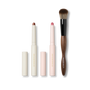 Cream Contour Stylus, pink Blush Stylus and a dual-ended wood-handled makeup brush on black — Victoria Beckham Beauty trio.