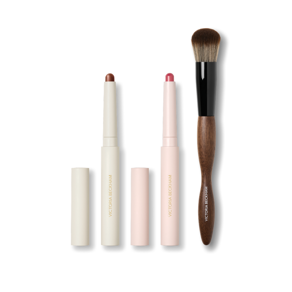 Cream Contour Stylus, pink Blush Stylus and a dual-ended wood-handled makeup brush on black — Victoria Beckham Beauty trio.