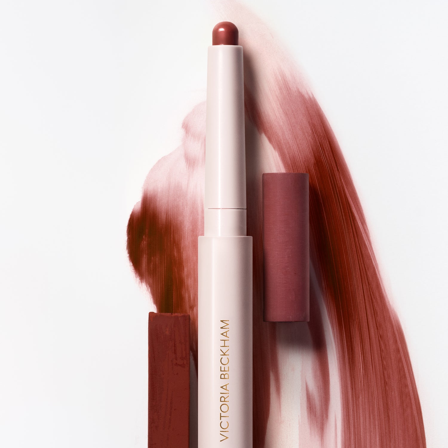 Cream stylus in a wine-rose shade beside its mauve cap with a terracotta cream swatch by Victoria Beckham Beauty.