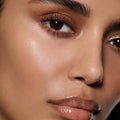 Close-up of a tan-complexion eye with cocoa-brown lashes and glossy lips — Vast Lash Cocoa and Posh Balm Soleil.