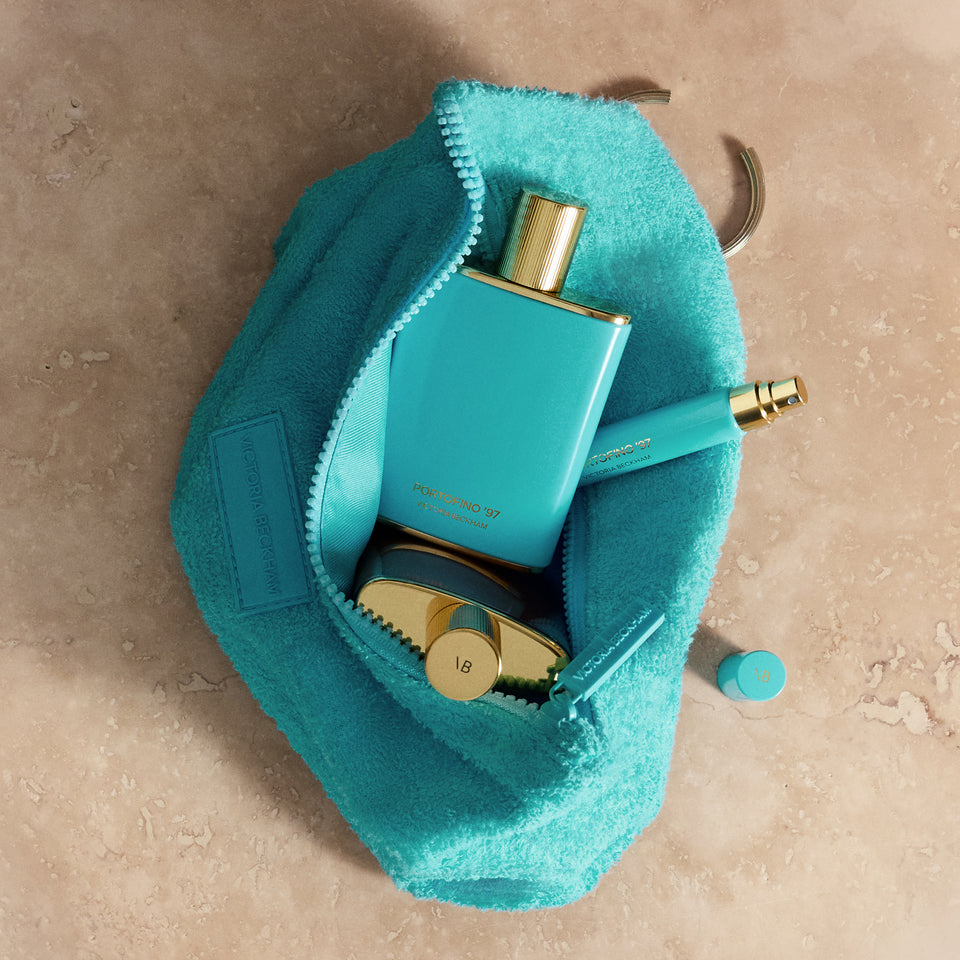 Open turquoise terry GWP pouch with Portofino '97 fragrance and atomizer on travertine — Victoria Beckham Beauty.