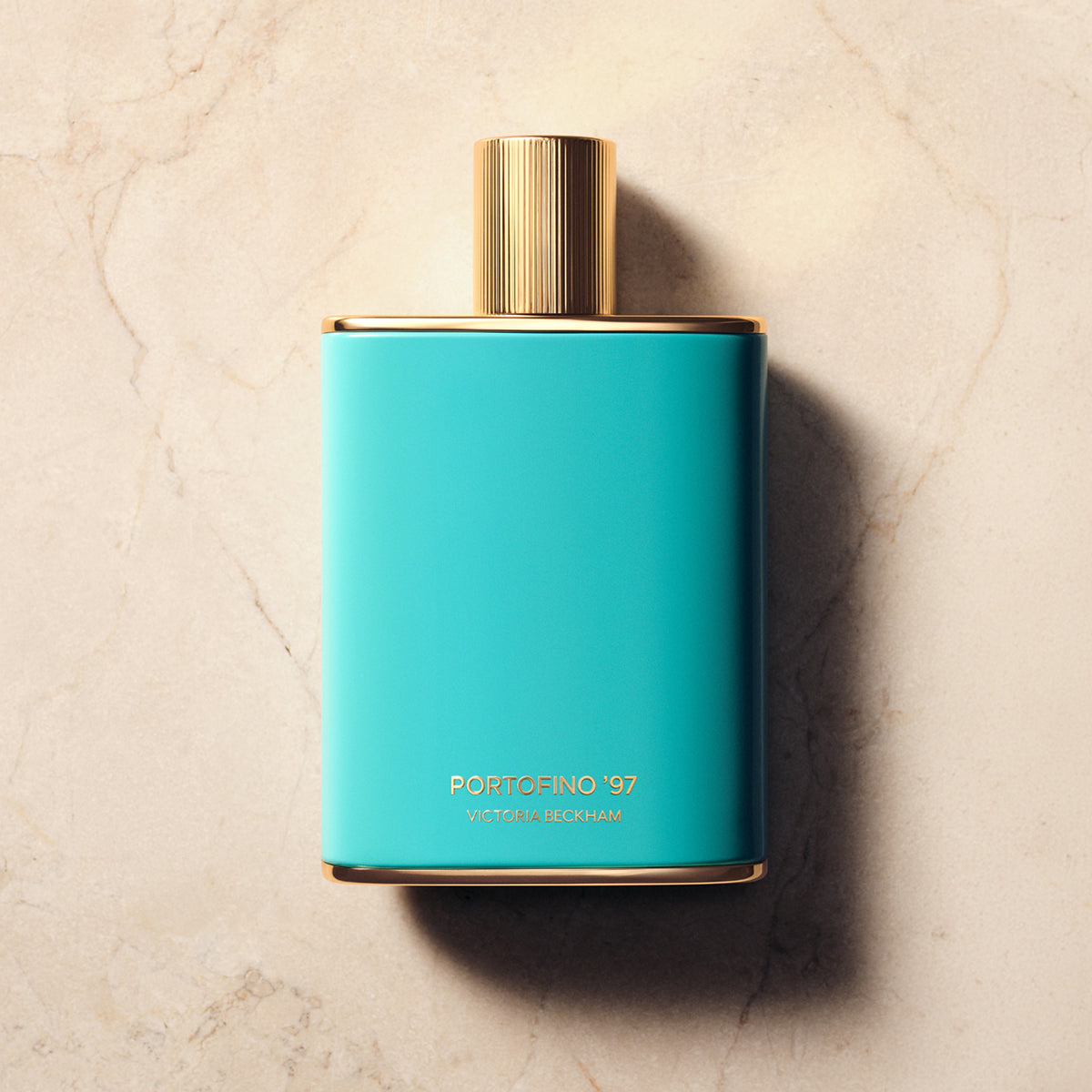 Turquoise Portofino '97 bottle with a fluted gold cap on cream marble — the fragrance by Victoria Beckham Beauty.