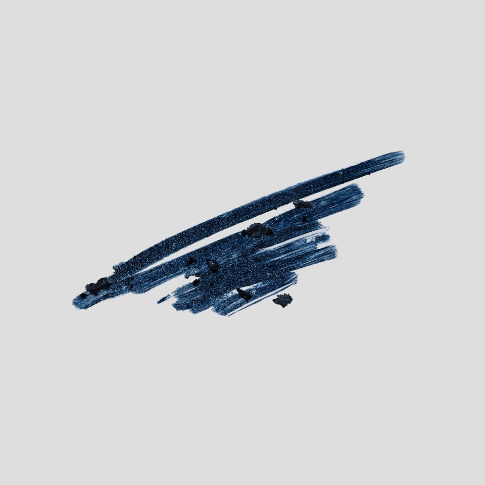 A textured, metallic dark blue glitter makeup swatch showing a thick, diagonal brush stroke on a solid light gray background.