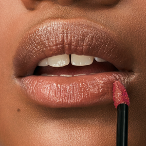 An image of a model's slightly open mouth, applying lip gloss to the bottom lip.