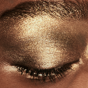 Close-up image of a model's eyelid with a shimmery golden eyeshadow.