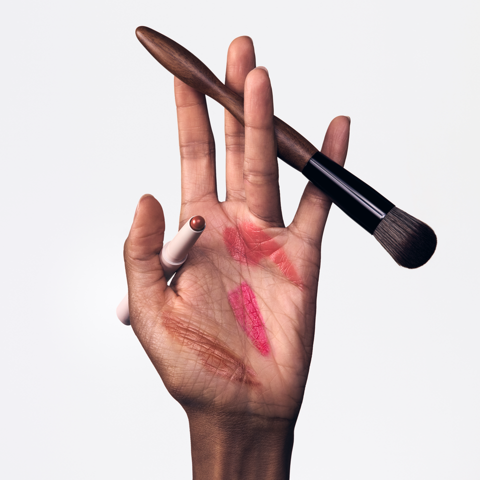 Open hand cradling makeup brush with Sienna and Rossa Blush Stylus swatches and bullet on palm — Victoria Beckham Beauty.