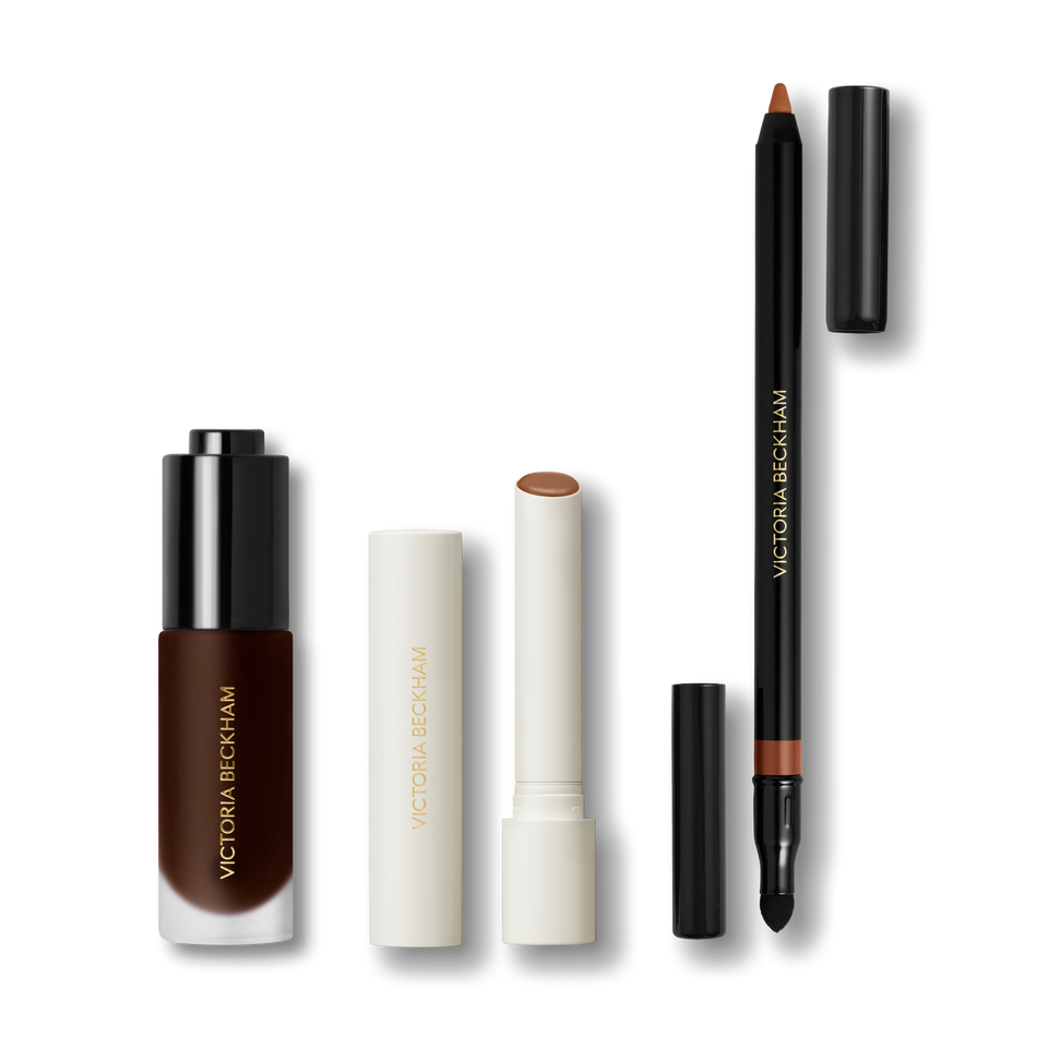The Foundation Drops, a cream-cased nude lipstick and a Lip Definer pencil on grey — Victoria Beckham Beauty Ultimate Trio.