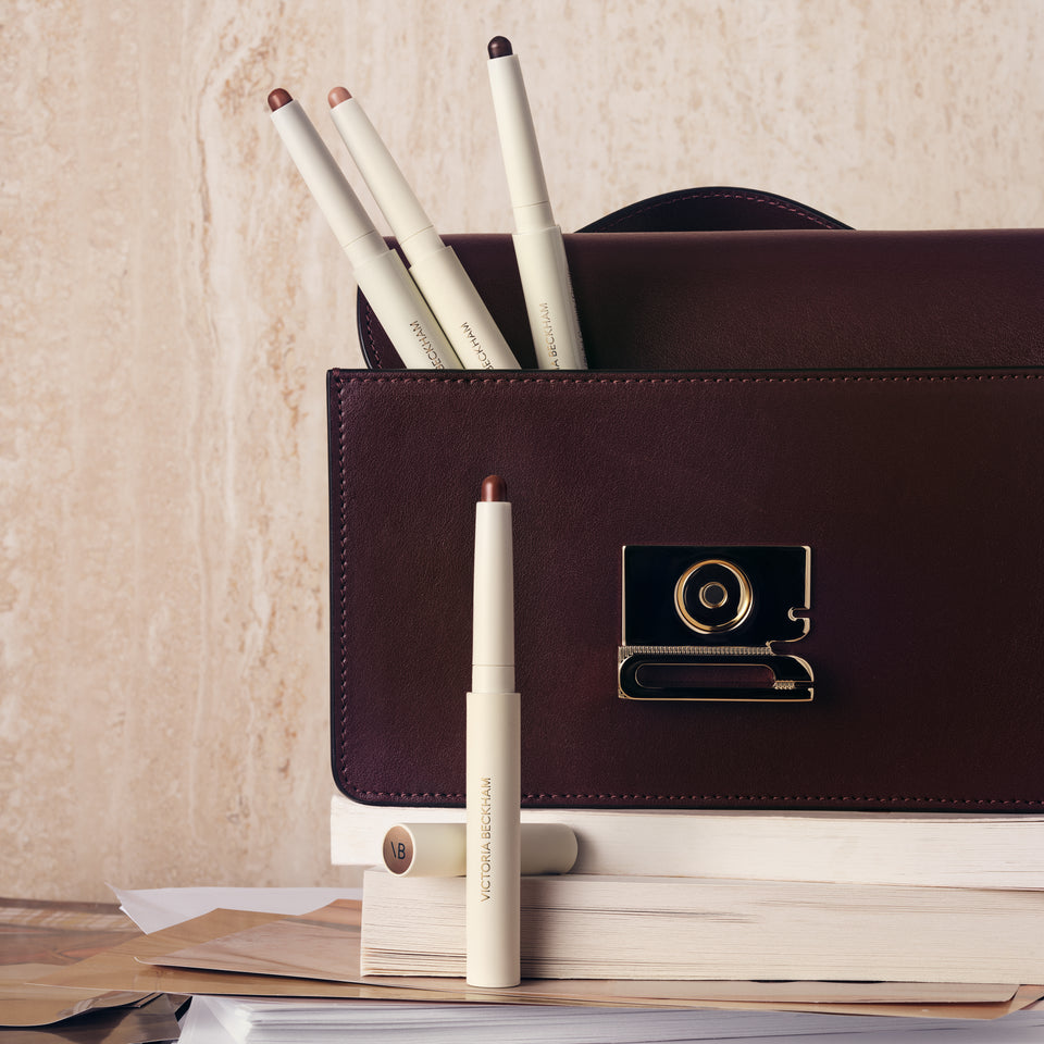 Cream Contour Stylus sticks tucked into a burgundy leather handbag — Victoria Beckham Beauty's cream contour pencil.