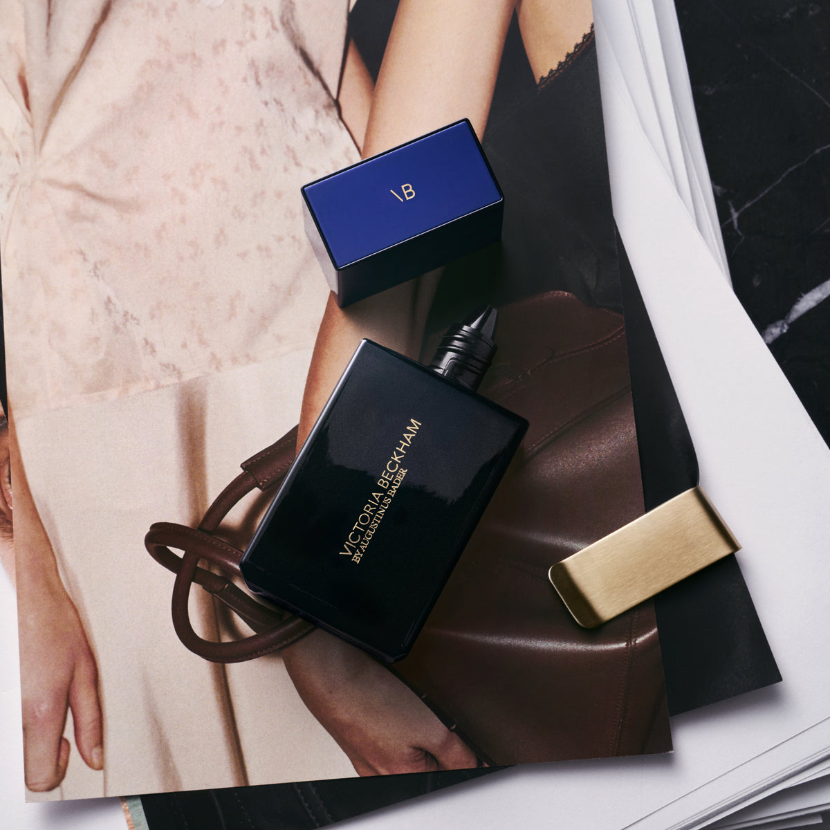 Dark navy dropper bottle and blue carton laid on magazine tear sheets — Victoria Beckham by Augustinus Bader.