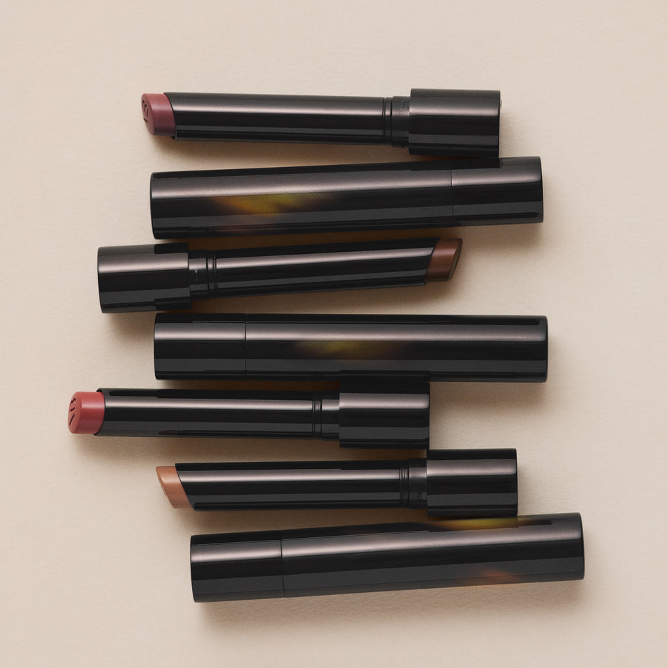 Seven Posh Lipstick tubes laid alternating on cream — nude, rose and cocoa bullets uncapped, by Victoria Beckham Beauty.