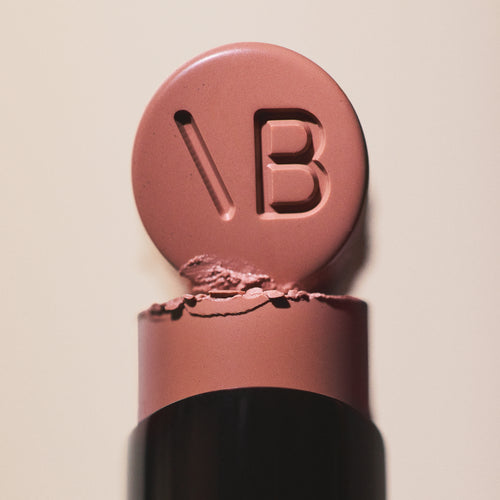 Macro of a rosewood Posh Lipstick bullet stamped with the Victoria Beckham monogram on its flat top.