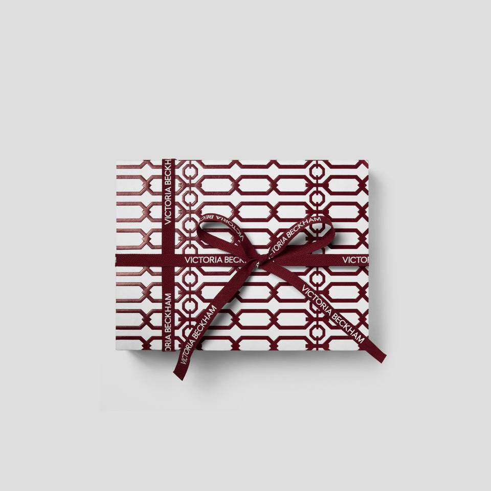 Top-down view of a Bordeaux Eye Kit gift box in burgundy trellis print, tied with a branded bow — Victoria Beckham Beauty.