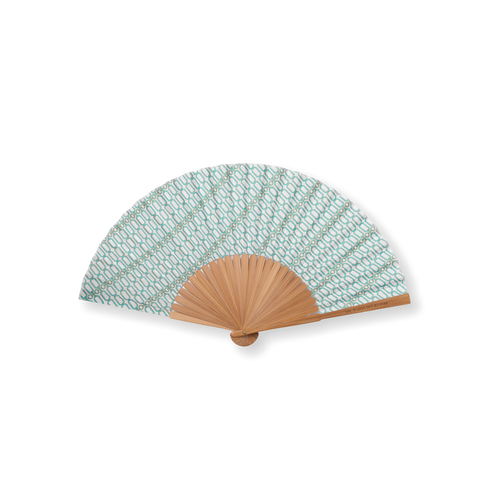 Open bamboo Portofino '97 hand fan in turquoise and gold chain-link print, Victoria Beckham signature on the spine.