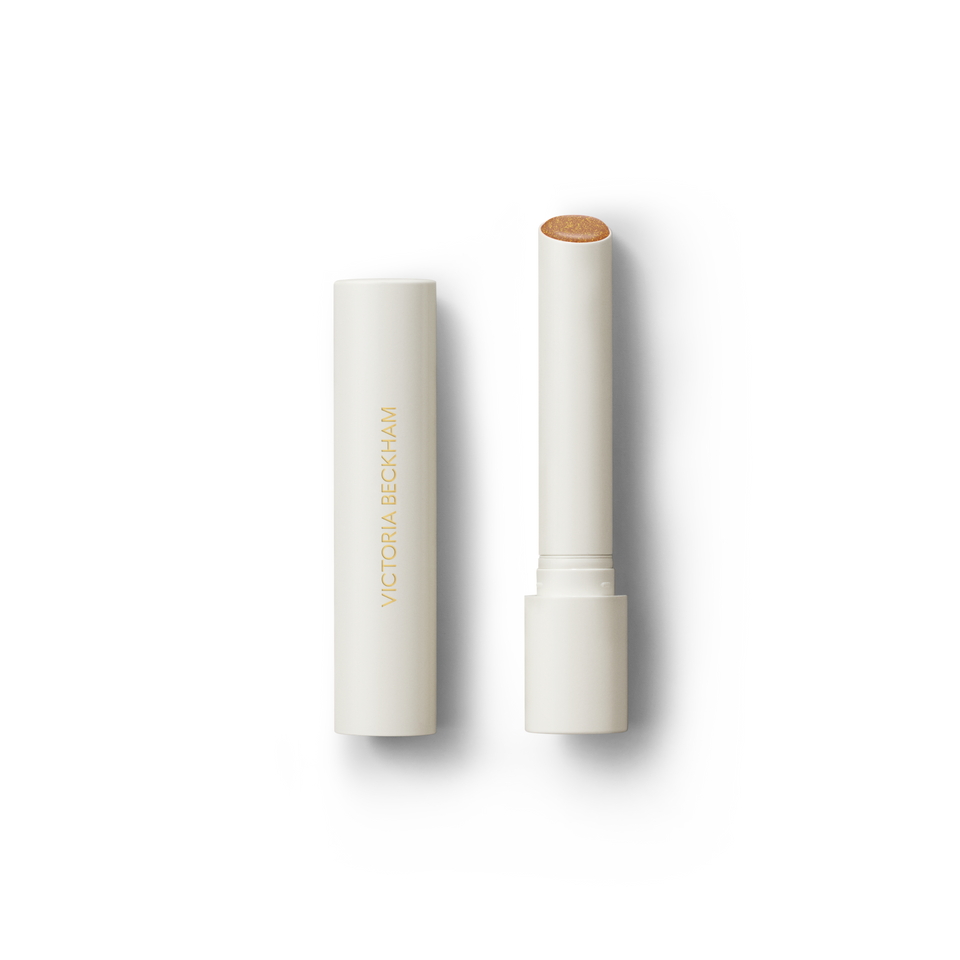Open Victoria Beckham Beauty Posh Balm in Soleil — cream tube and cap beside the golden bronze shimmer balm bullet.