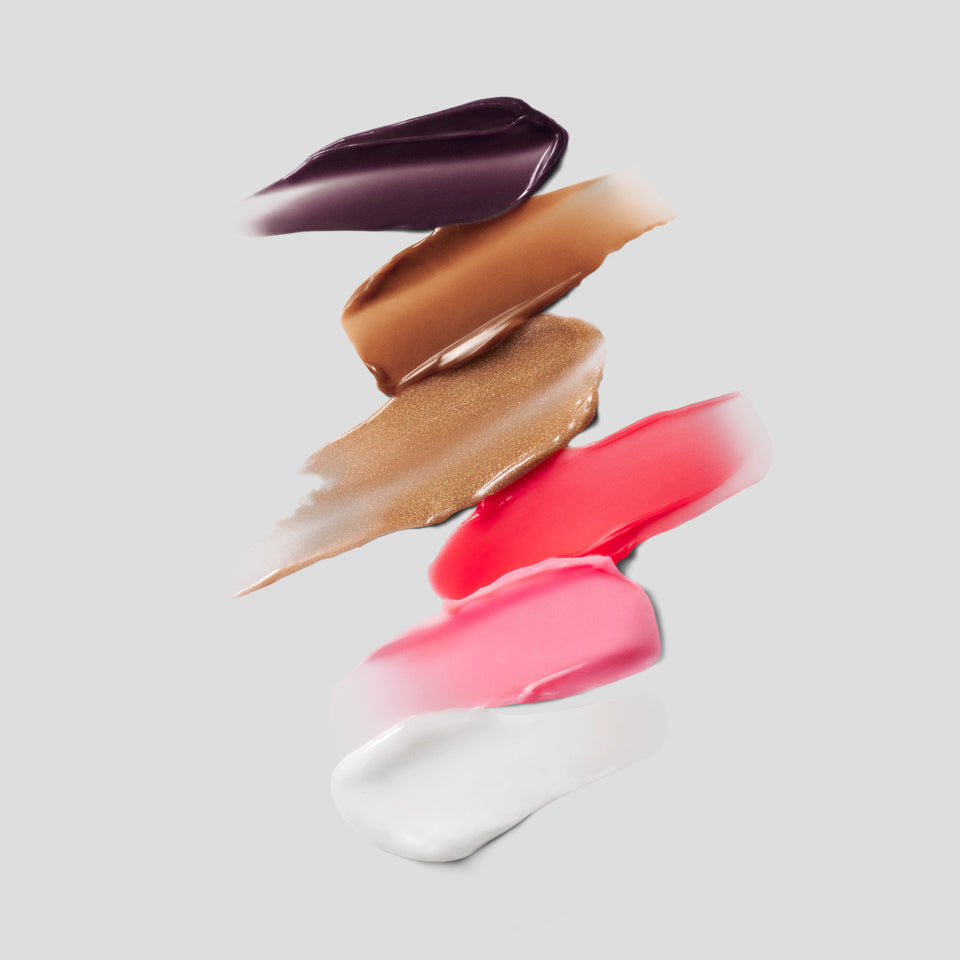 Six Posh Balm swatches on grey — plum, caramel, golden bronze, coral, pink and clear by Victoria Beckham Beauty.
